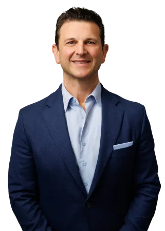 Smiling man in a blue blazer and light blue shirt standing against a transparent background.