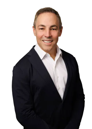 Smiling man in a white shirt and dark blazer posing confidently against a plain background