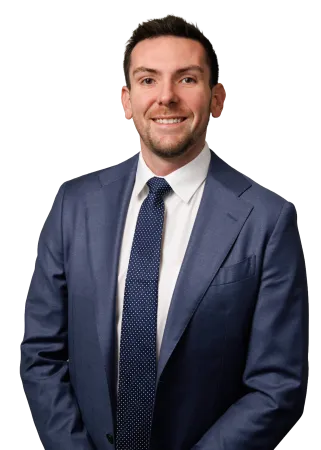Smiling man in blue suit and white shirt wearing a navy blue polka dot tie posing with hands folded.