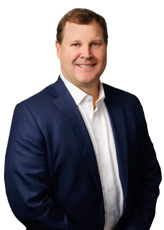 Smiling man in blue suit jacket and white shirt against a plain background, posing confidently.