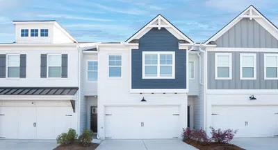 Modern townhouses with white and gray exteriors, multiple garages, and small landscaped bushes under a blue sky.