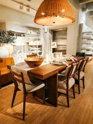 Modern wooden dining table set with cushioned chairs under large woven pendant light in showroom