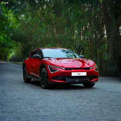 Red Kia EV6 electric car parked on cobblestone road surrounded by green trees and bamboo plants.