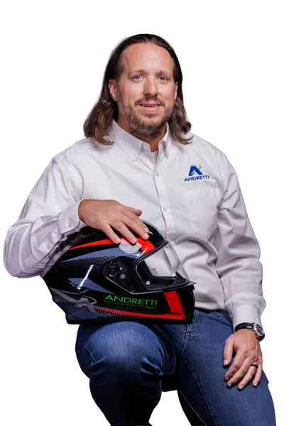Man in white Andretti shirt holding a black and red Andretti racing helmet with jeans.