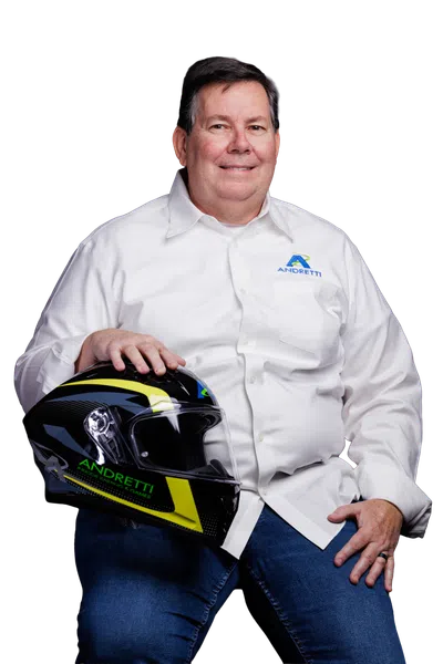 Man wearing a white Andretti shirt holding a black and yellow Andretti racing helmet while sitting.