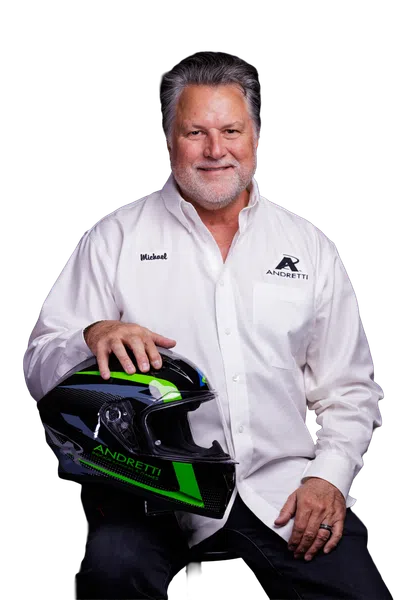 Smiling man in white Andretti shirt holding a black and green racing helmet against a black background