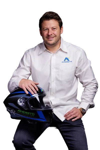 Man in white Andretti shirt holding a black and blue racing helmet with Andretti branding