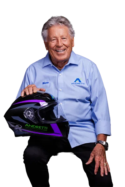 Elderly man in light blue Andretti shirt holding a racing helmet with purple and green accents, smiling.