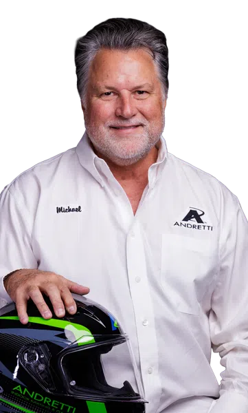 Smiling man in white Andretti shirt holding a black and green racing helmet against a black background