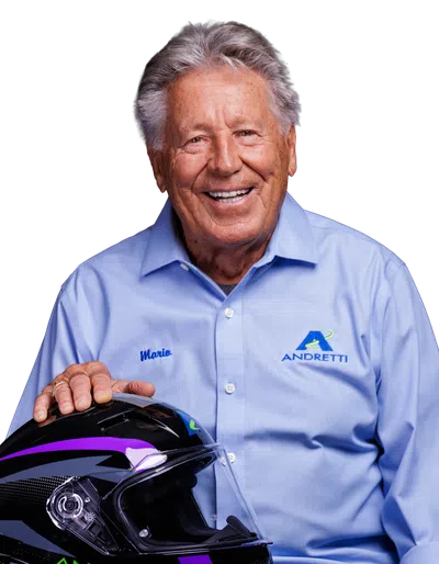 Elderly man in light blue Andretti shirt holding a racing helmet with purple and green accents, smiling.