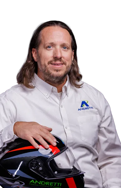 Man in white Andretti shirt holding a black and red Andretti racing helmet with jeans.