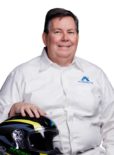 Man wearing a white Andretti shirt holding a black and yellow Andretti racing helmet while sitting.
