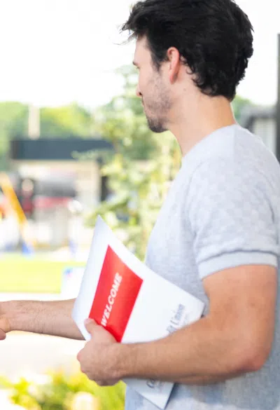 Two men shaking hands outside a building, one holding a welcome brochure, smiling and greeting.