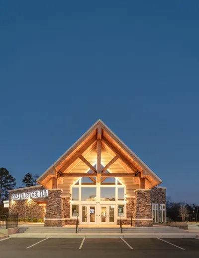 Coosa Valley Credit Union building with stone pillars and large glass windows lit up at dusk under a clear blue sky