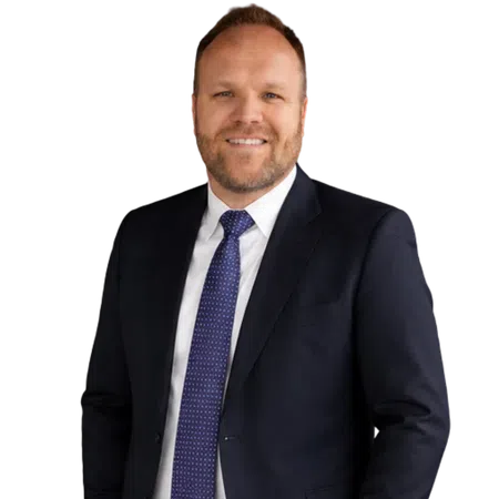 Smiling man in dark suit, white shirt, and blue patterned tie against black background.