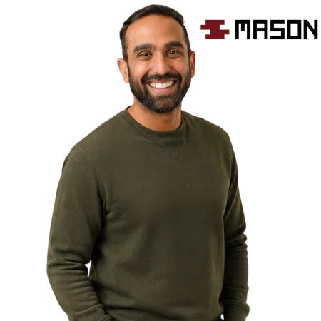 Smiling man in an olive green sweater standing with hands in pockets against a white background