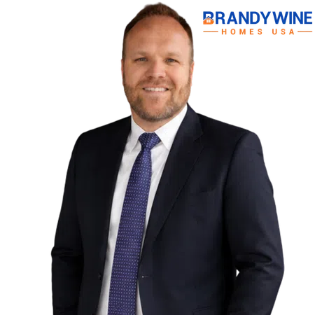 Smiling man in dark suit and blue tie standing with Brandywine Homes USA logo on black background