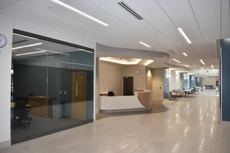Modern office lobby with curved reception desk, glass-walled conference room, and seating area along bright hallway.