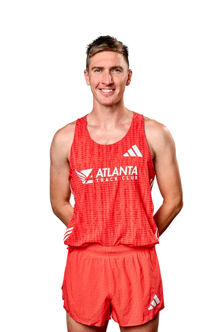 Smiling male runner wearing red Atlanta Track Club uniform with Adidas logos on tank top and shorts.