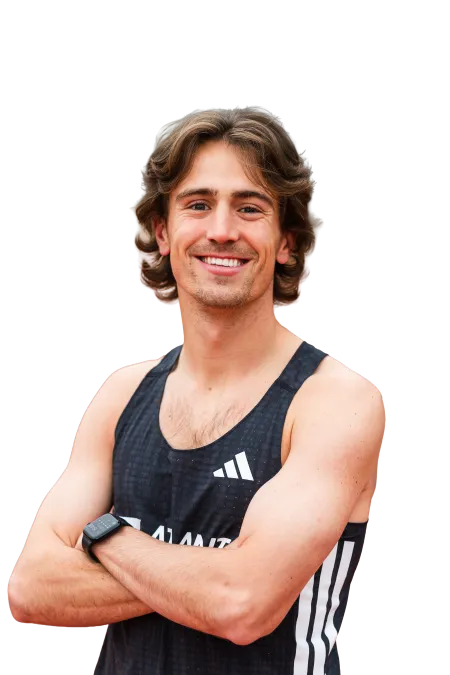Smiling young male athlete with wavy hair wearing a black Adidas sports tank top and smartwatch, arms crossed.