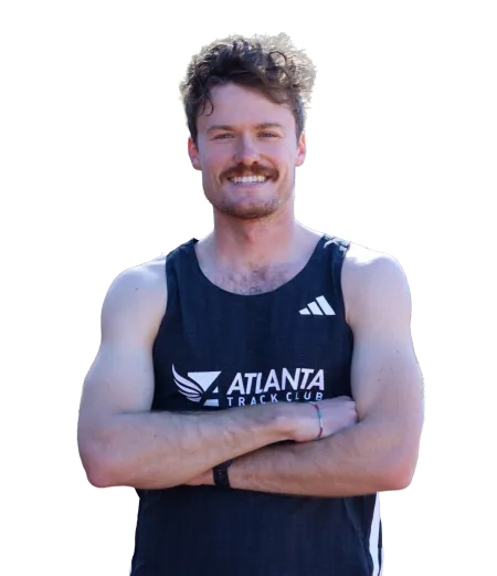 Smiling male athlete with curly hair wearing Atlanta Track Club black sleeveless top, arms crossed