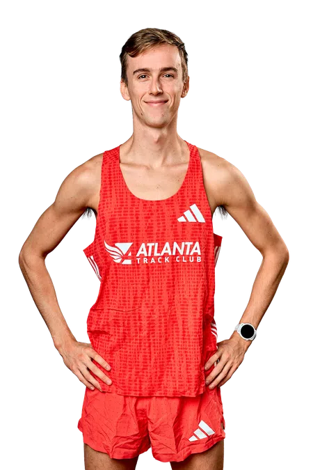 Smiling male athlete in red Atlanta Track Club running uniform with smartwatch posing hands on hips.