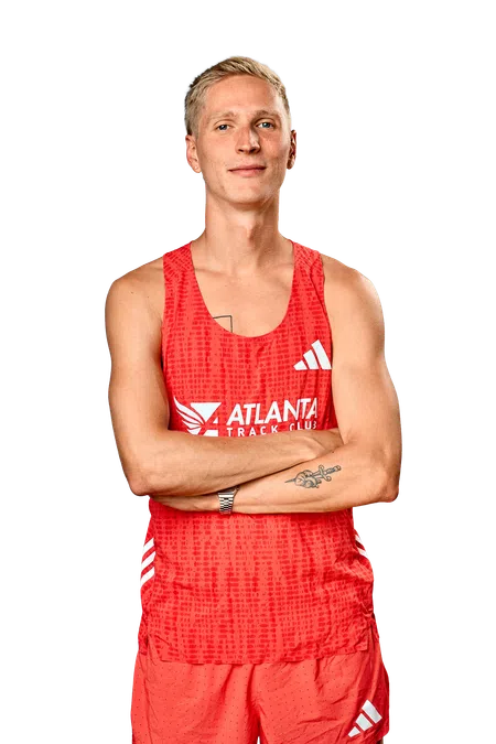 Young male athlete in red Atlanta Track Club running gear with tattoos and short blonde hair crossing arms