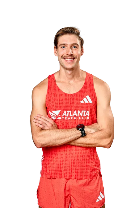 Smiling male athlete wearing red Atlanta Track Club running outfit with a watch, arms crossed.