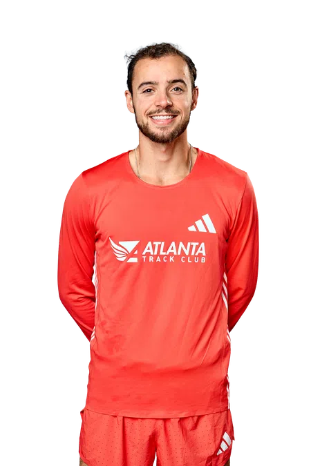 Smiling male athlete wearing red Atlanta Track Club running gear with Adidas logos on top and shorts.