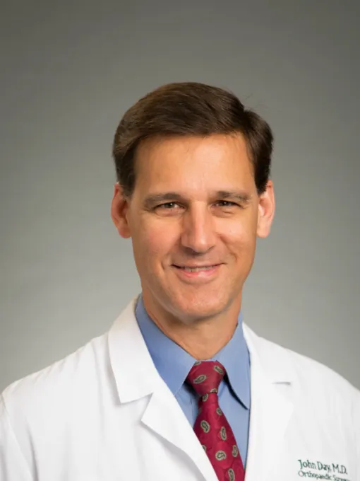 Portrait of a male doctor in a white coat with a red patterned tie and blue shirt smiling against gray background