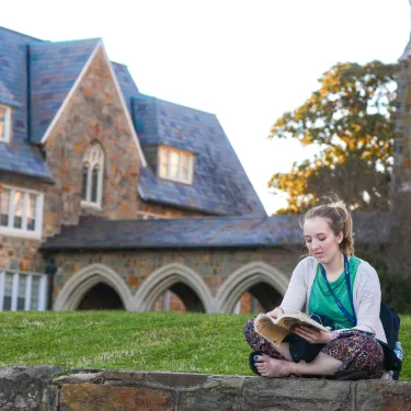 a student sitting in the courtyard of the Ford Buildings at Berry College Reading a Book