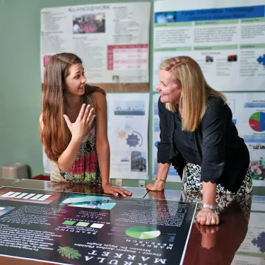 Berry student and professor talk while leaning over a board on a table