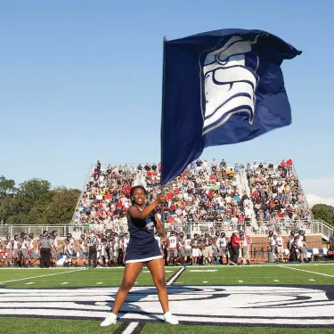 Berry student holds a flag on a football field in front of packed stands