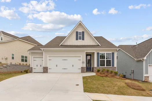 Modern single-story house with a large driveway, three-car garage, and manicured front lawn under a blue sky.