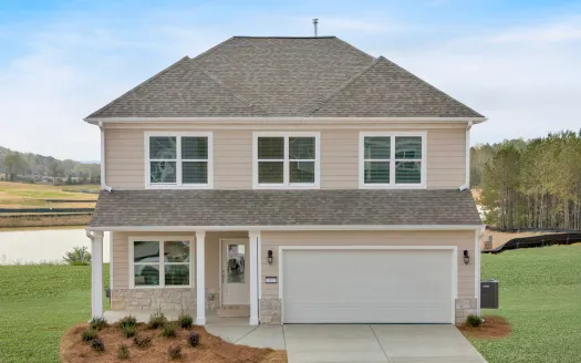 Two-story beige house with white trim, large garage, and landscaped front yard against a rural backdrop.
