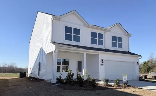 New two-story white house with a large garage under clear blue sky and sparse landscaping around it