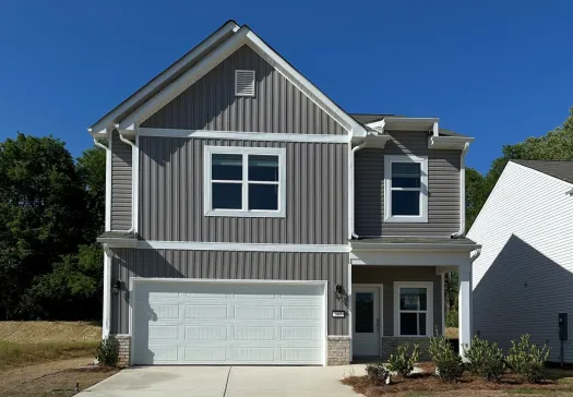 New two-story gray house with white garage door, concrete driveway, and small front yard landscaping under clear blue sky.