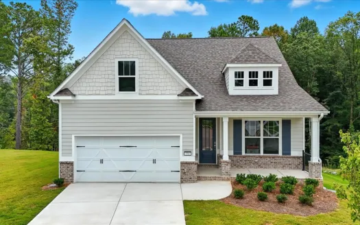 Modern two-story gray house with attached garage, front porch, manicured lawn, and surrounding trees under a blue sky.