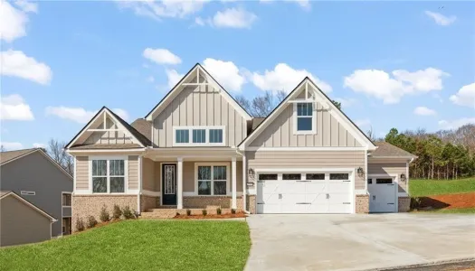 Modern single-story beige house with gabled roof, front porch, three-car garage, and green lawn under a blue sky.