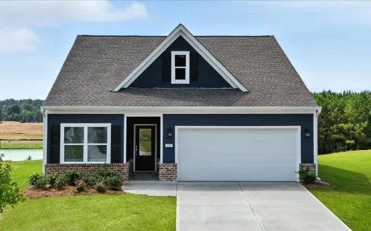 Modern navy blue house with brick accents, white garage door, dormer window, and lush green lawn under a clear sky