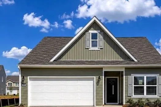Modern single-story house with gray siding, white garage door, large driveway, and well-kept lawn under a blue sky.