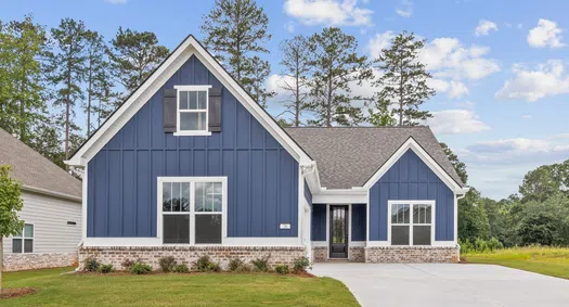 Modern blue house with white trim, large windows, brick foundation, and a spacious driveway under a partly cloudy sky.