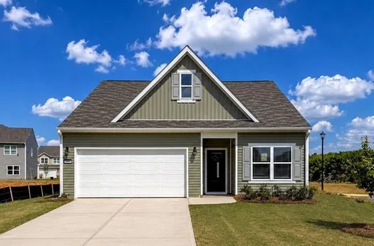 Modern single-story house with gray siding, white garage door, large driveway, and well-kept lawn under a blue sky.