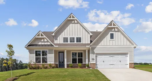 Modern single-story house with white siding, gabled roof, attached garage, and manicured lawn under a blue sky.