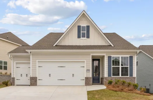 Modern single-story house with a large driveway, two-car garage, and manicured lawn under a blue sky.
