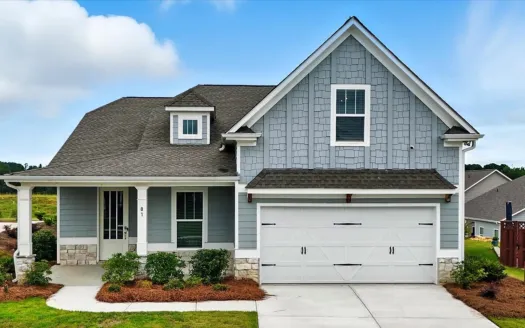 Modern two-story gray house with white garage door, green bushes, and a concrete driveway under a blue sky.
