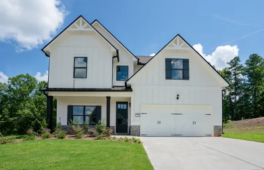 Modern two-story white house with black accents, large garage, front porch, and landscaped lawn under blue sky.