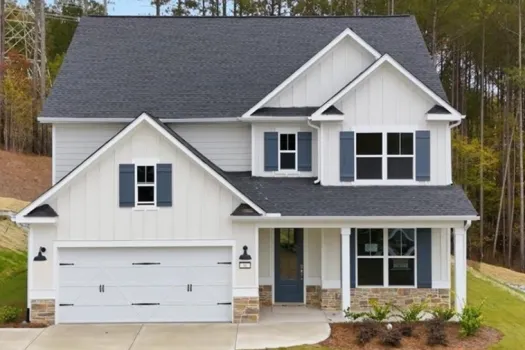 Modern two-story white house with gray shutters, stone accents, and a two-car garage in a wooded area.