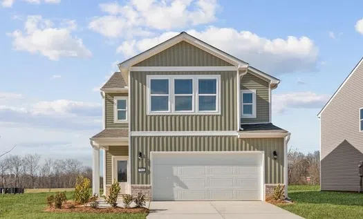 Modern two-story house with gray vertical siding, white garage door, and a green lawn under a blue sky.
