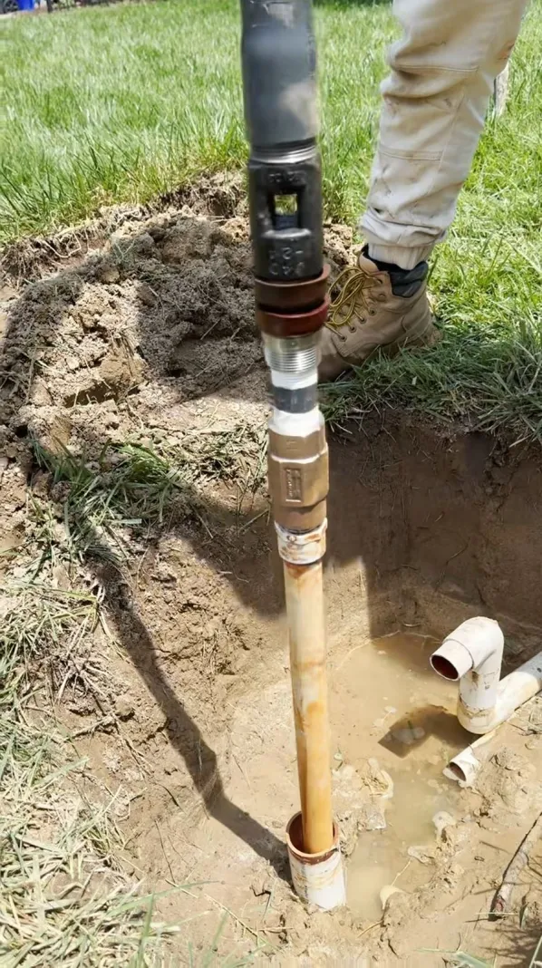 Close-up of a PVC pipe with a connection being installed in wet soil.